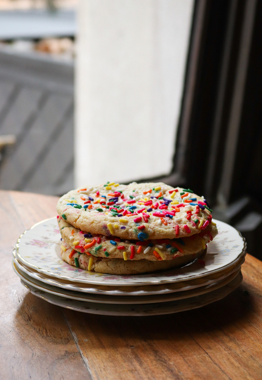Stack of two colorful sprinkled cookies on floral plates, resting on a wooden table.