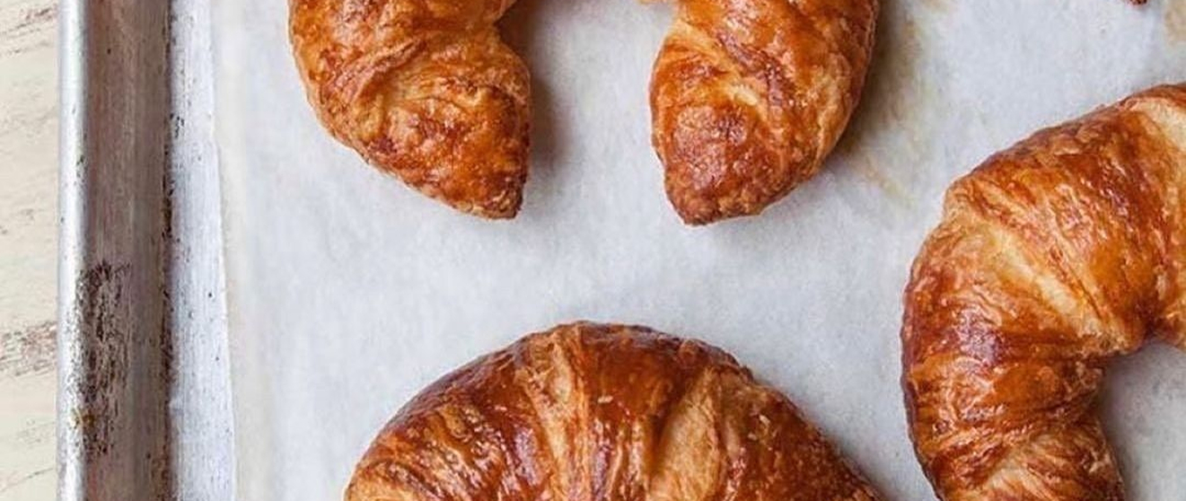 Golden-brown croissants with flaky layers, arranged on a parchment-lined baking sheet.