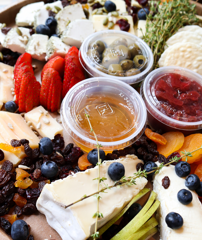 Assorted cheeses, fruits, nuts, and drizzled honey on a platter with garnishes.