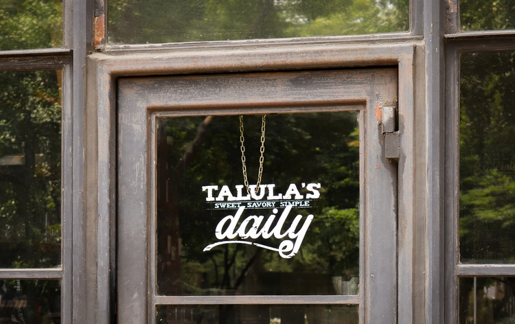 Restaurant window with "Talula's Daily" sign, suggesting sweet, savory, simple, in a rustic setting.